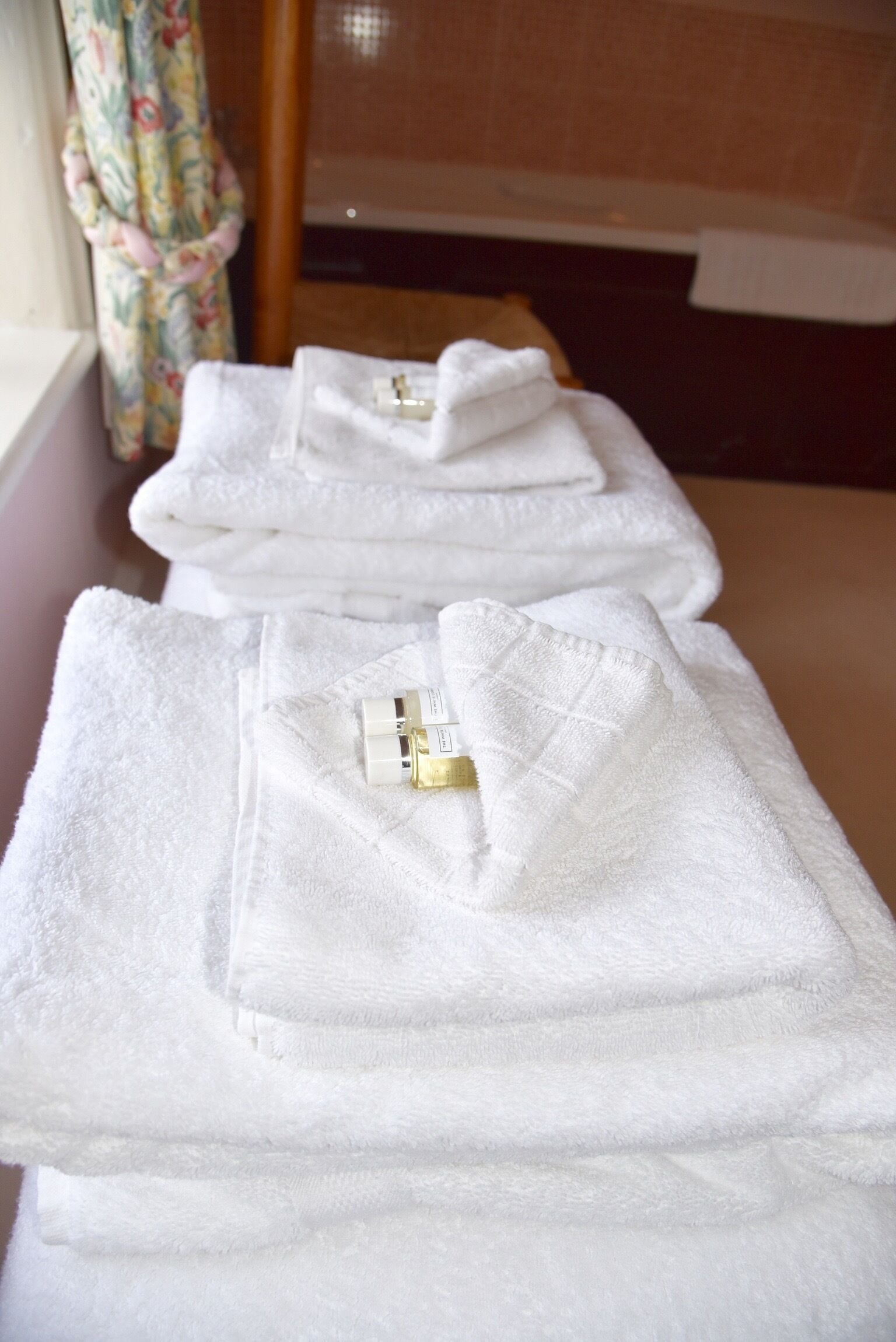 A stack of white towels with a gold-colored object on one of them, placed on a surface near a window with a curtain.