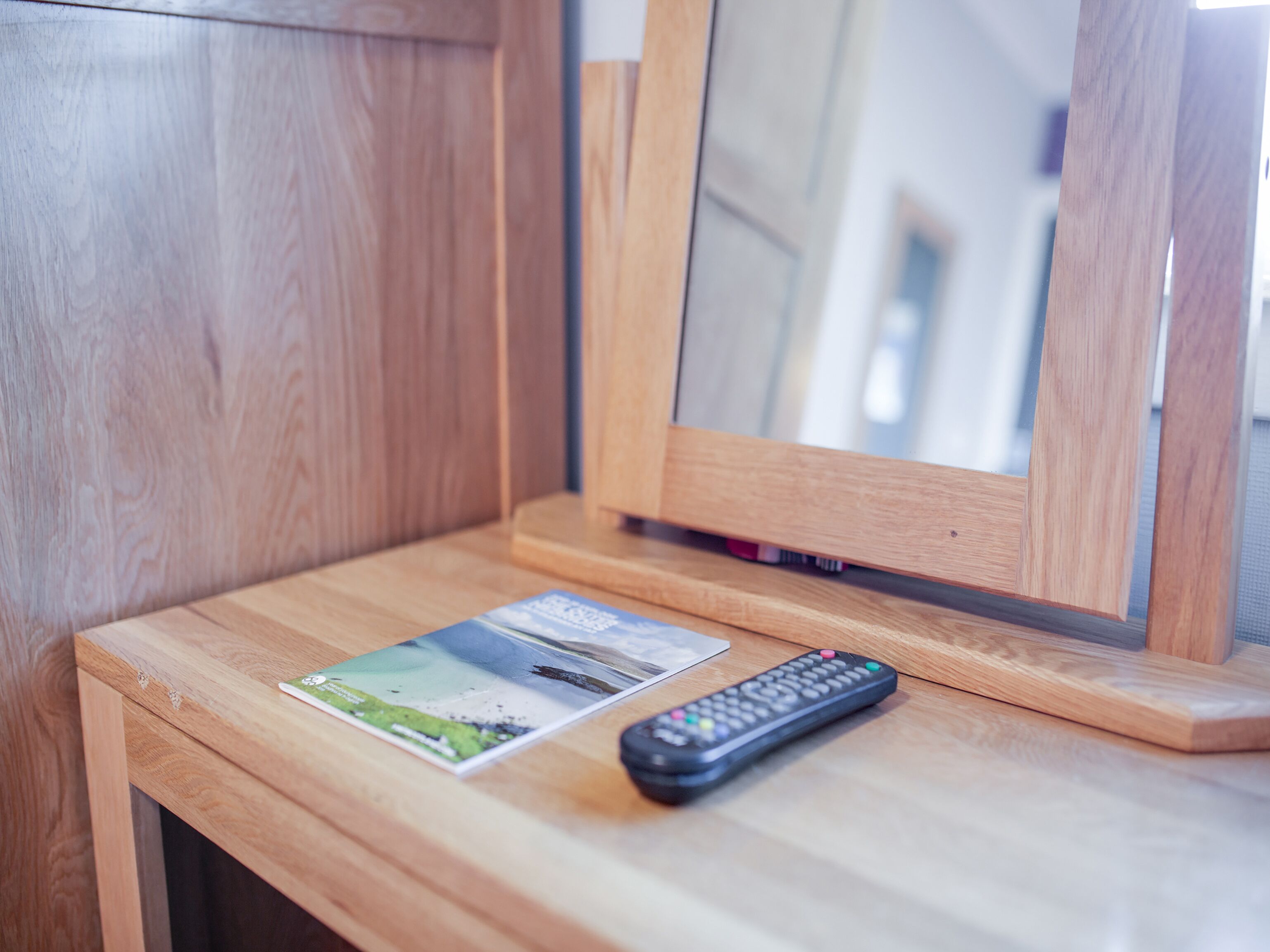 A wooden bedside table with a remote control and a brochure.