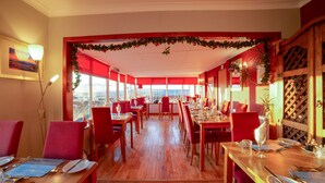 Ein Restaurant mit roten Stühlen und Tischen, großen Fenstern und Blick auf die Stadt.