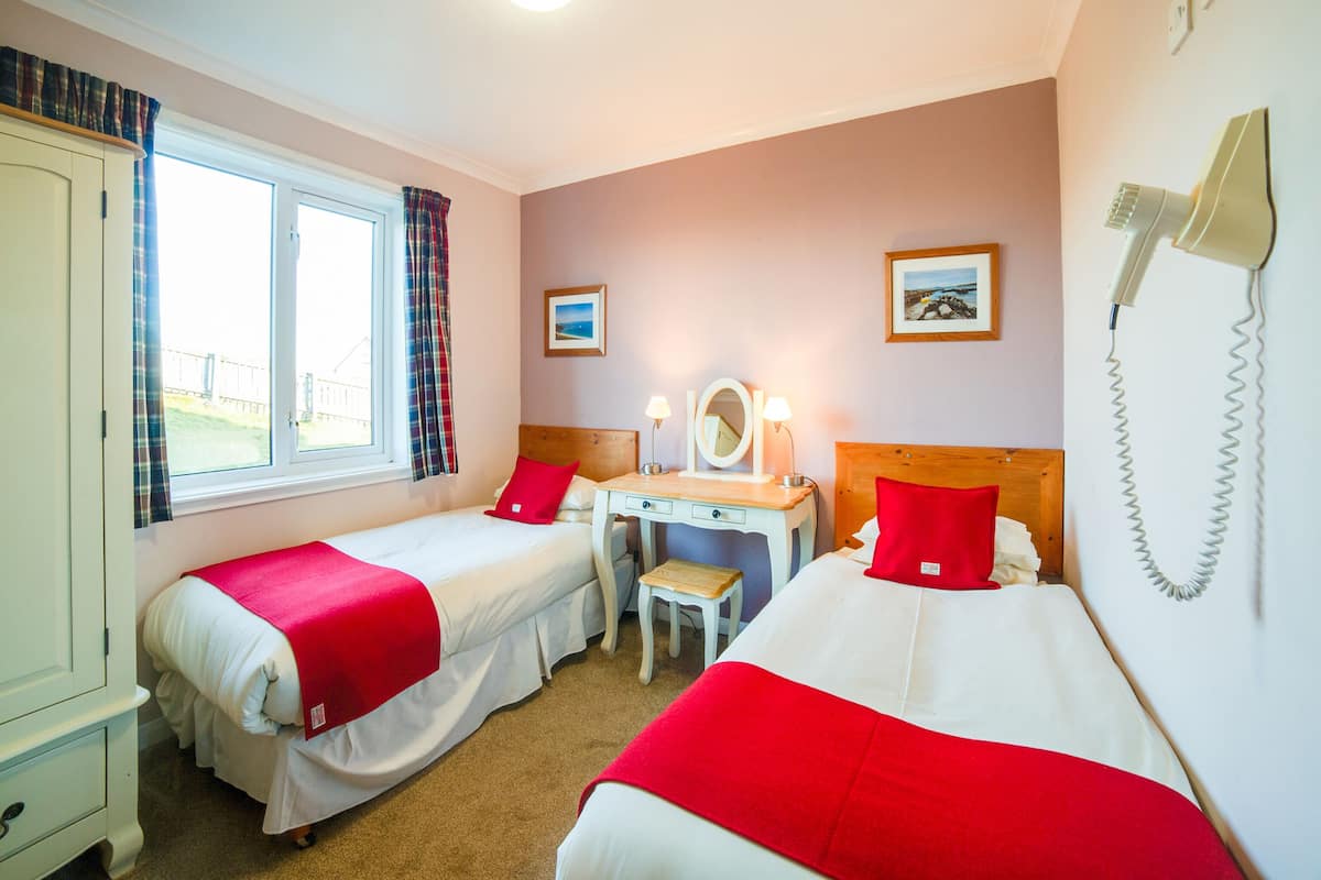A hotel room with two beds, a desk, a chair, a wardrobe, and a window with curtains.