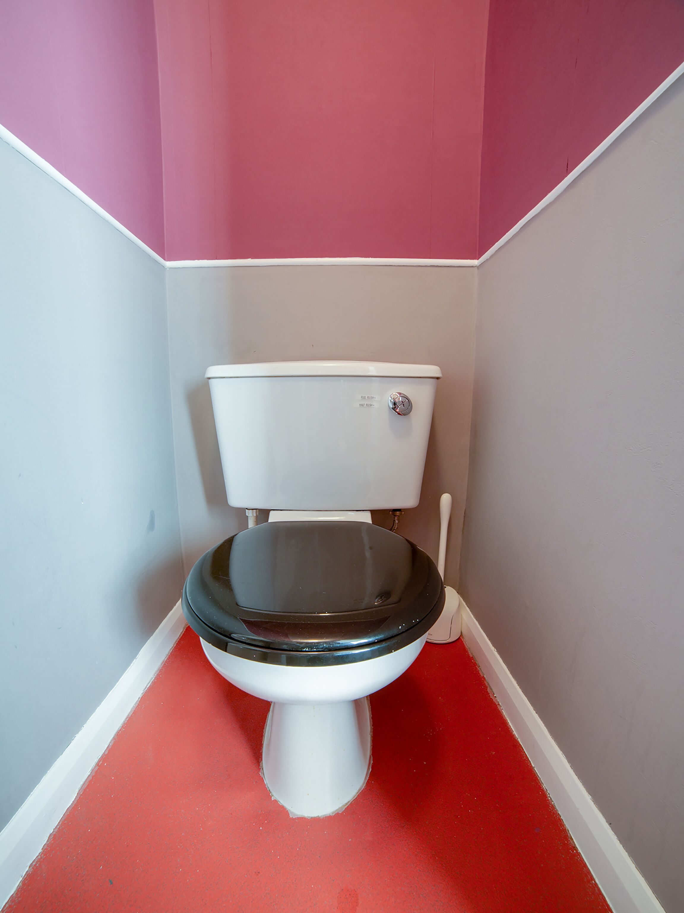 A toilet in a corner with a red floor and pink walls.