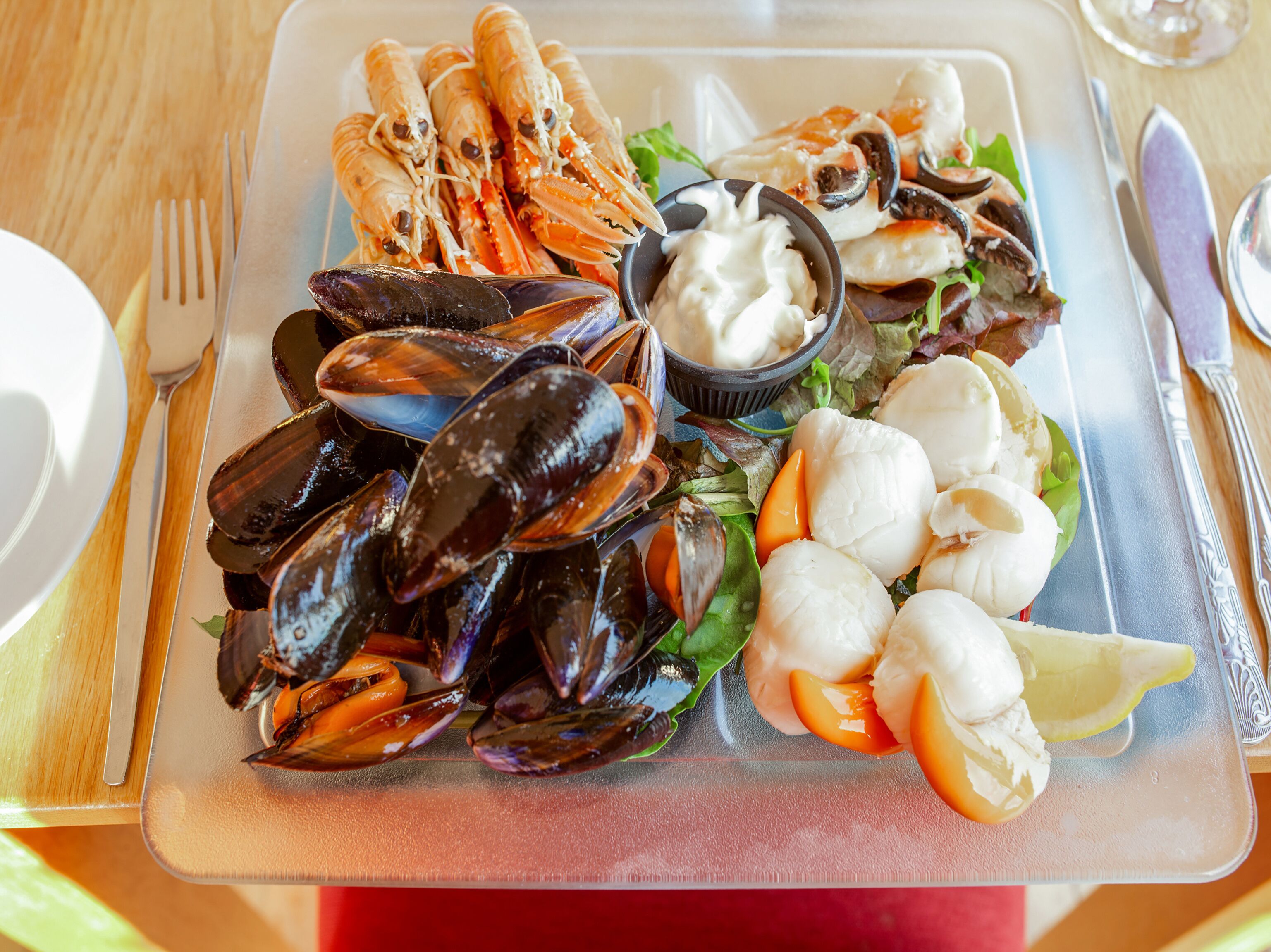 A seafood platter with mussels, lobster, and clams, accompanied by a small bowl of sauce and lemon slices.
