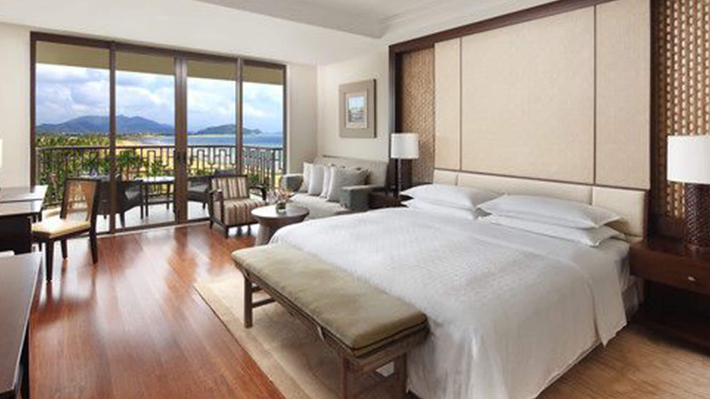 Habitación de hotel con una cama grande, un escritorio, una silla, una mesita y un balcón con vistas a las montañas.