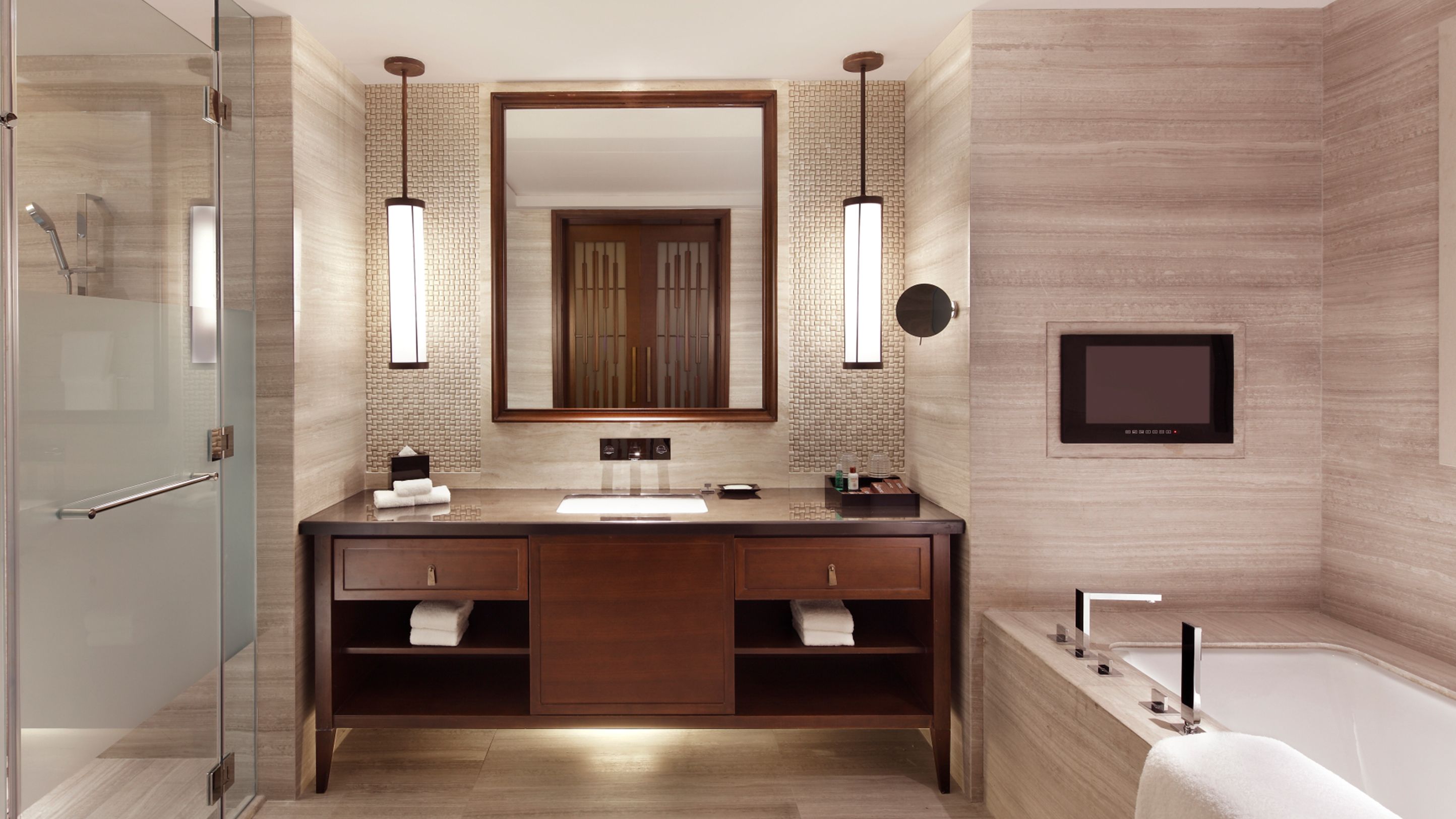 A modern bathroom with a glass shower enclosure, a double vanity with a large mirror, and a built-in TV.