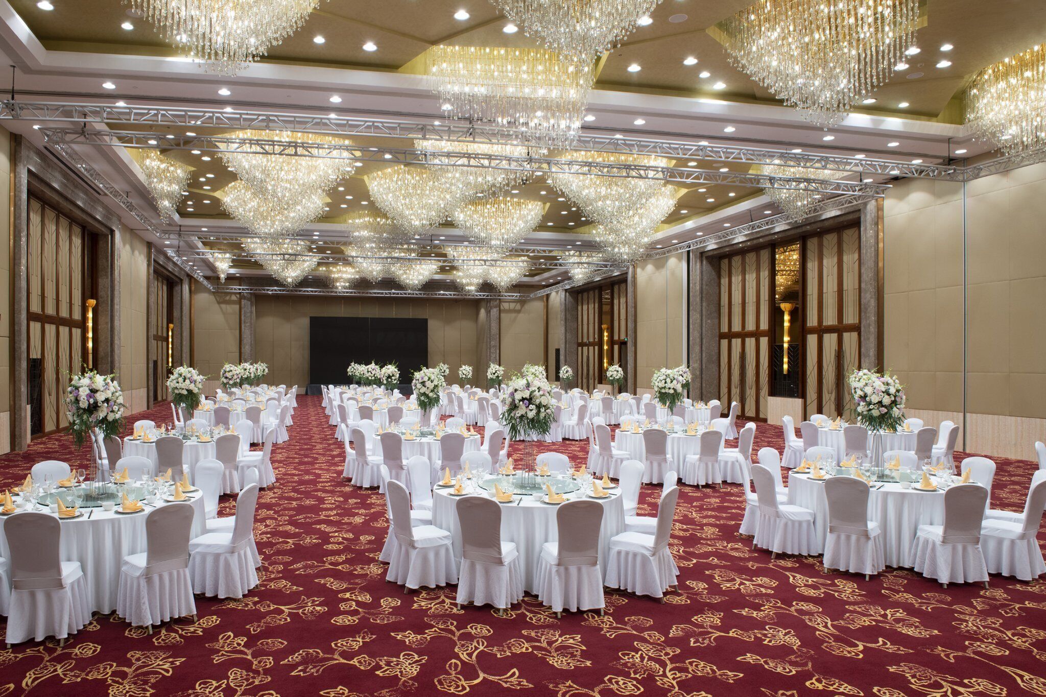 A banquet hall with round tables, white chairs, and floral centerpieces.