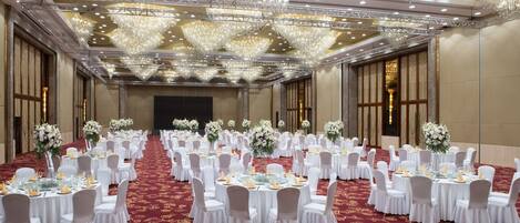 A banquet hall with round tables, white chairs, and floral centerpieces.