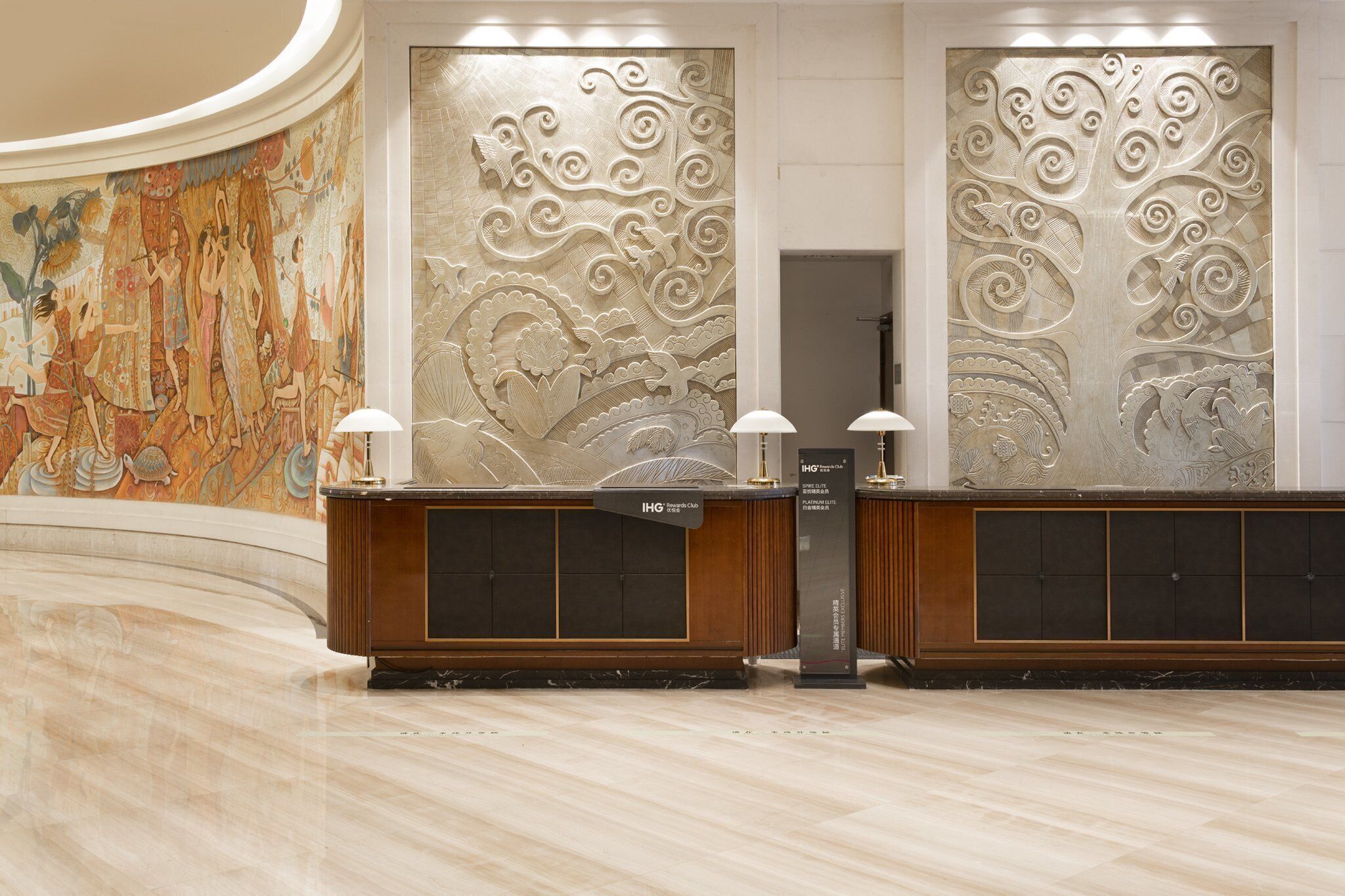 A hotel reception area with a marble floor, a reception desk with a sign for IHG Rewards Club, and a large decorative wall with intricate patterns.