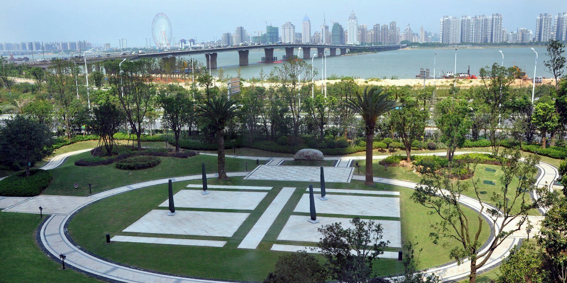 Un parque arbolado con senderos y una gran masa de agua al fondo.