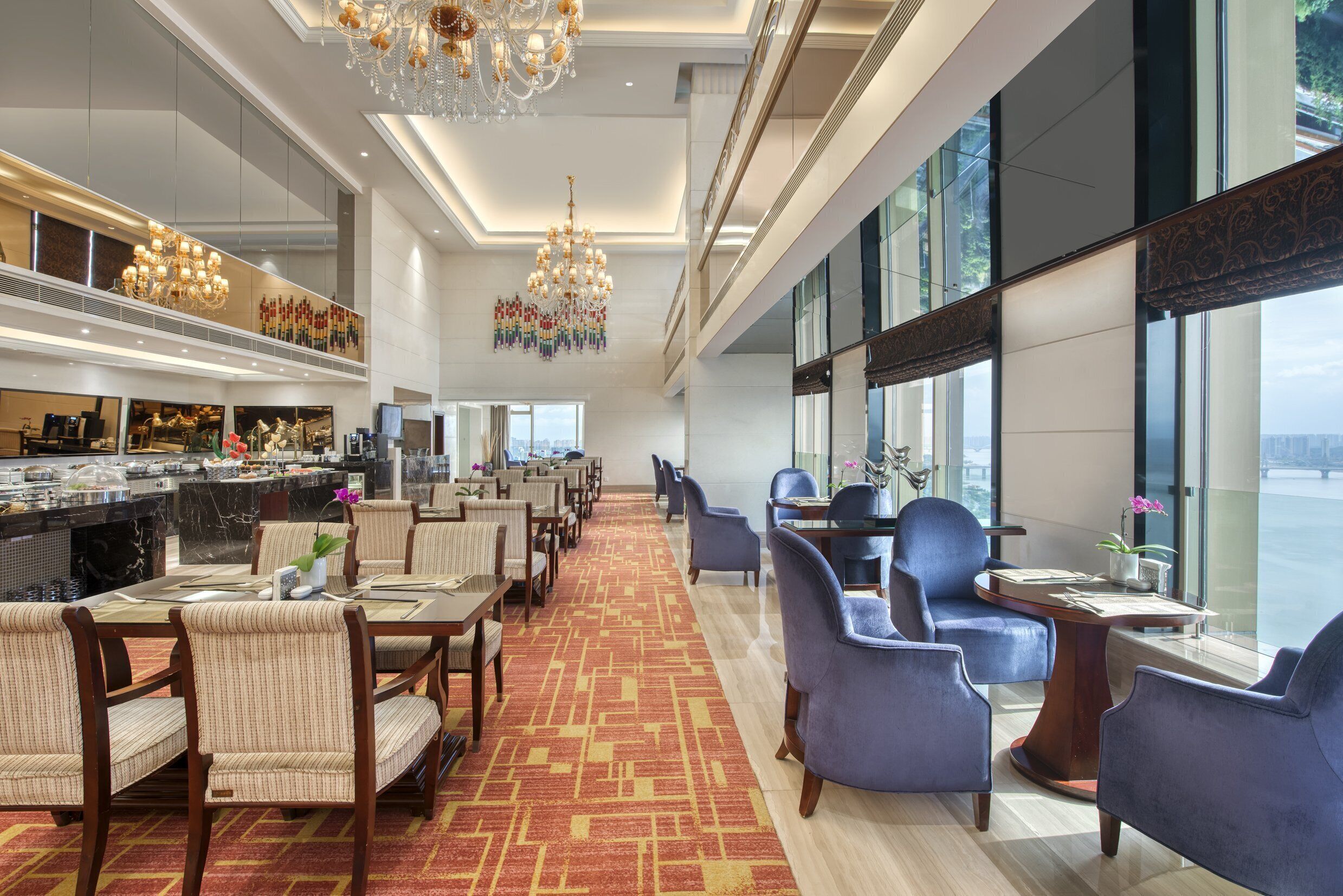 Un hall de hotel con zona de buffet, asientos y grandes ventanales con vistas.