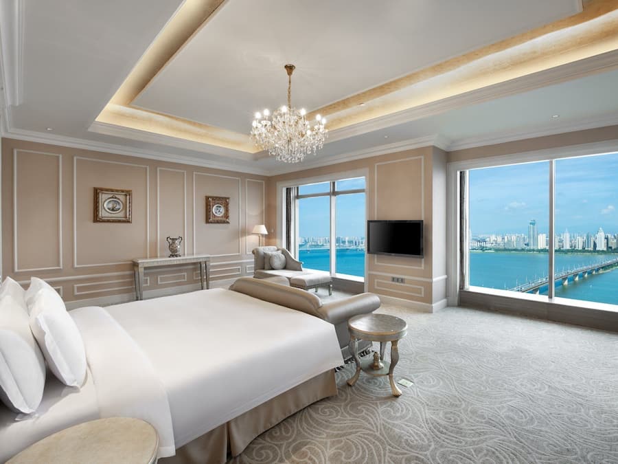 Amplia habitación de hotel con una cama grande, zona de estar, televisión y vistas a la ciudad y al agua.