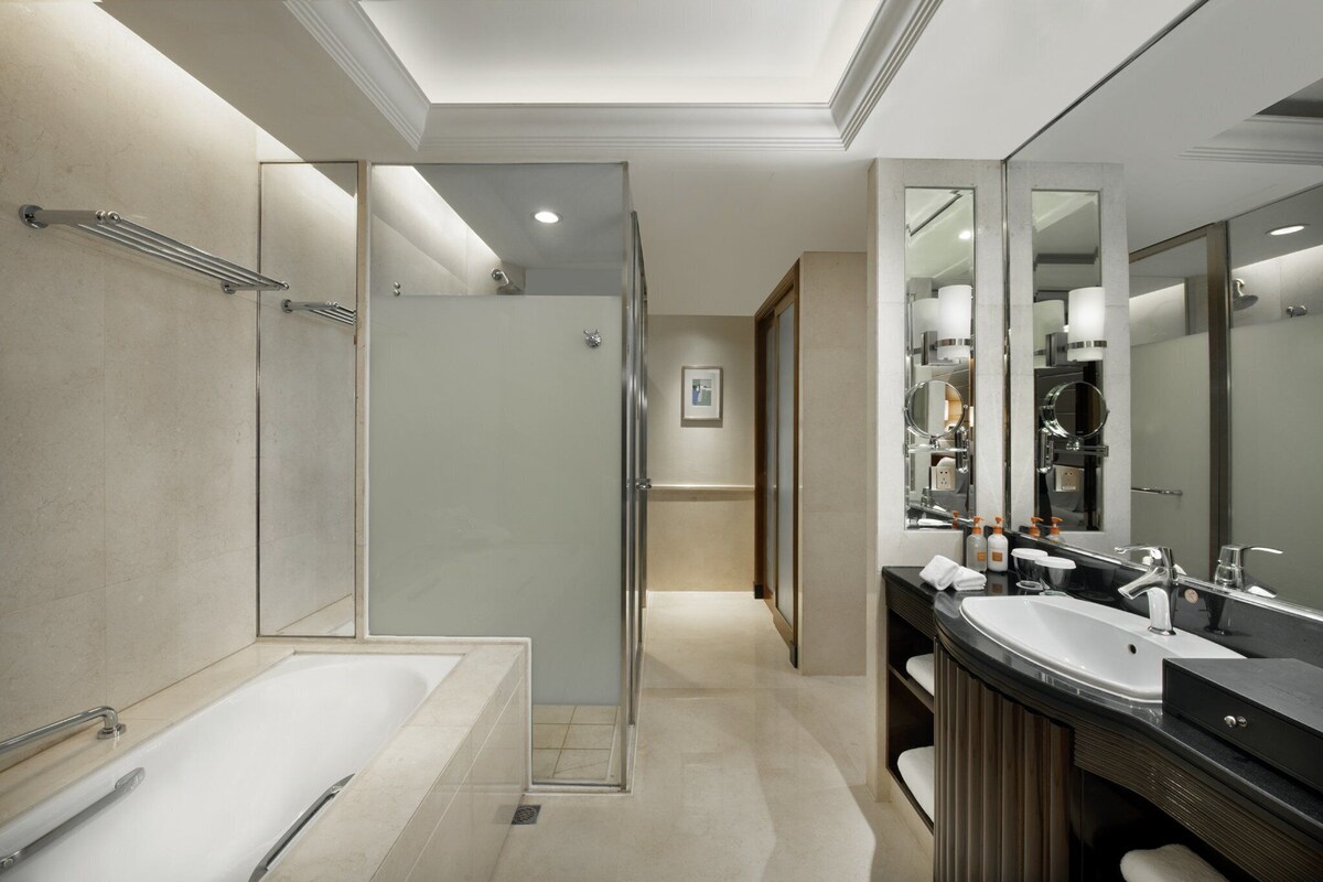 A modern bathroom with a glass-enclosed shower, a large bathtub, and a vanity with a double sink.