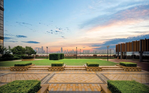 A landscaped courtyard with a view of a city skyline at sunset.