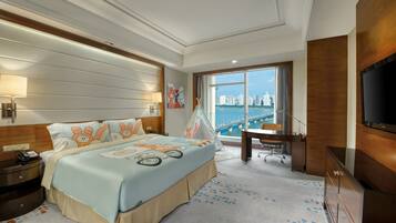 A hotel room with a large bed, a desk, a chair, a TV, and a view of a cityscape.