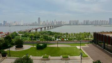 A riverside park with a bridge, greenery, and a city skyline in the background.