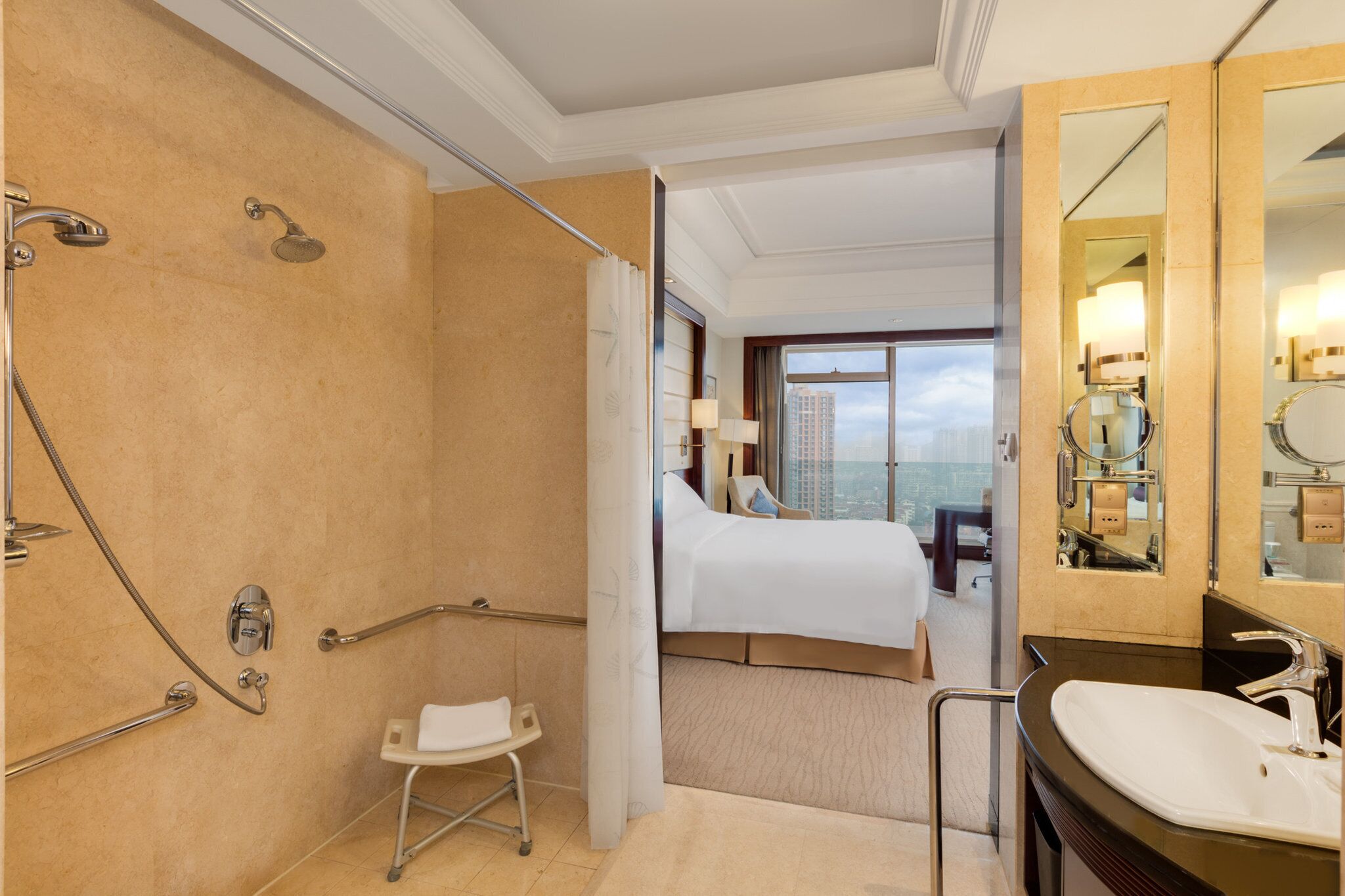 Een hotelkamer met een douche, een bed, uitzicht op de stad en een badkamer met een wastafel en spiegel.