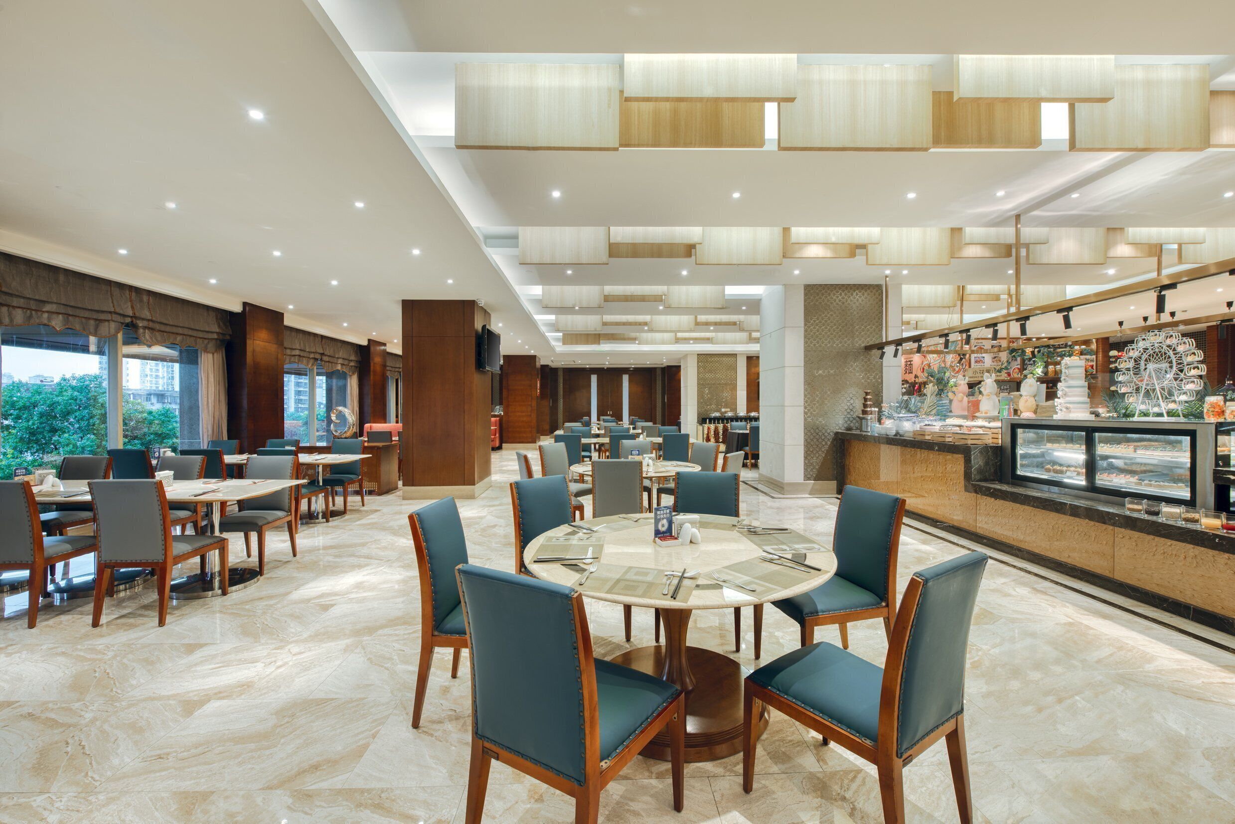 A spacious hotel dining area with multiple tables and chairs, a central round table, and a dessert display.