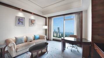 A hotel room with a large window, a sofa, a desk, and a TV.
