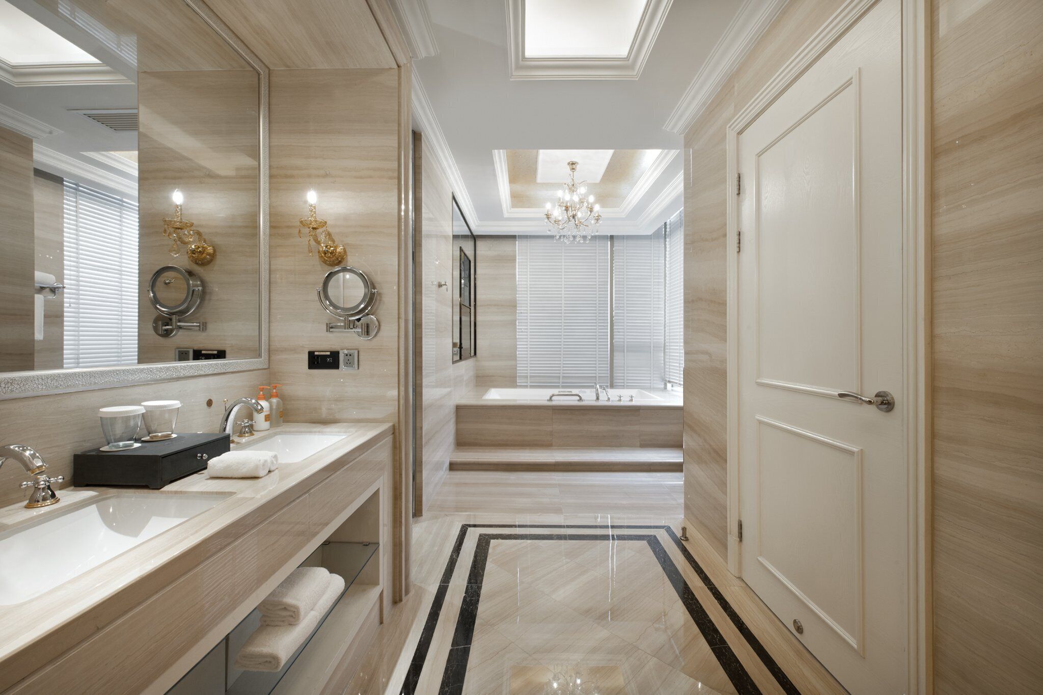 A modern bathroom with a large mirror, two sinks, a chandelier, and a view to a shower area.