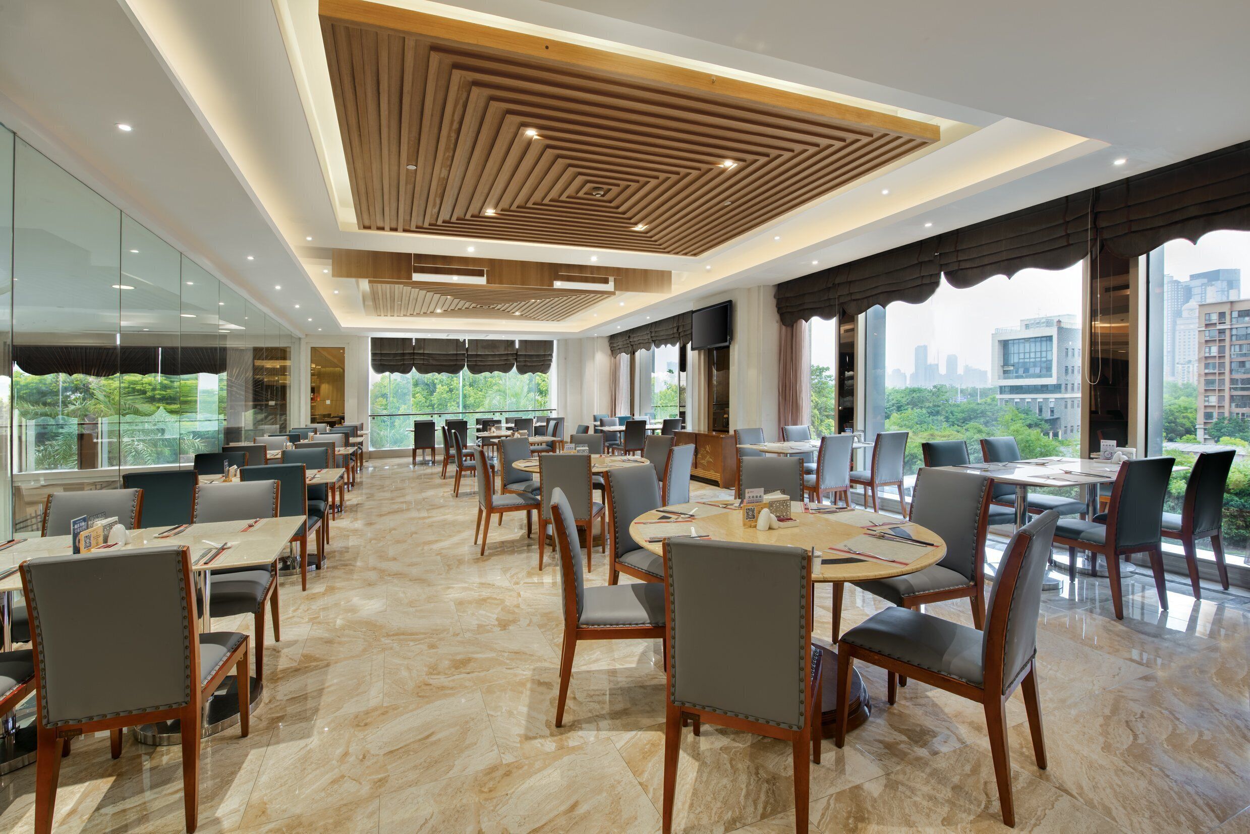 A spacious restaurant with high ceilings, modern lighting, and large windows offering a city view.