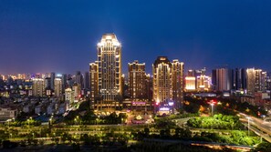 A cityscape at night with illuminated high-rise buildings, a well-lit central plaza, and surrounding greenery.