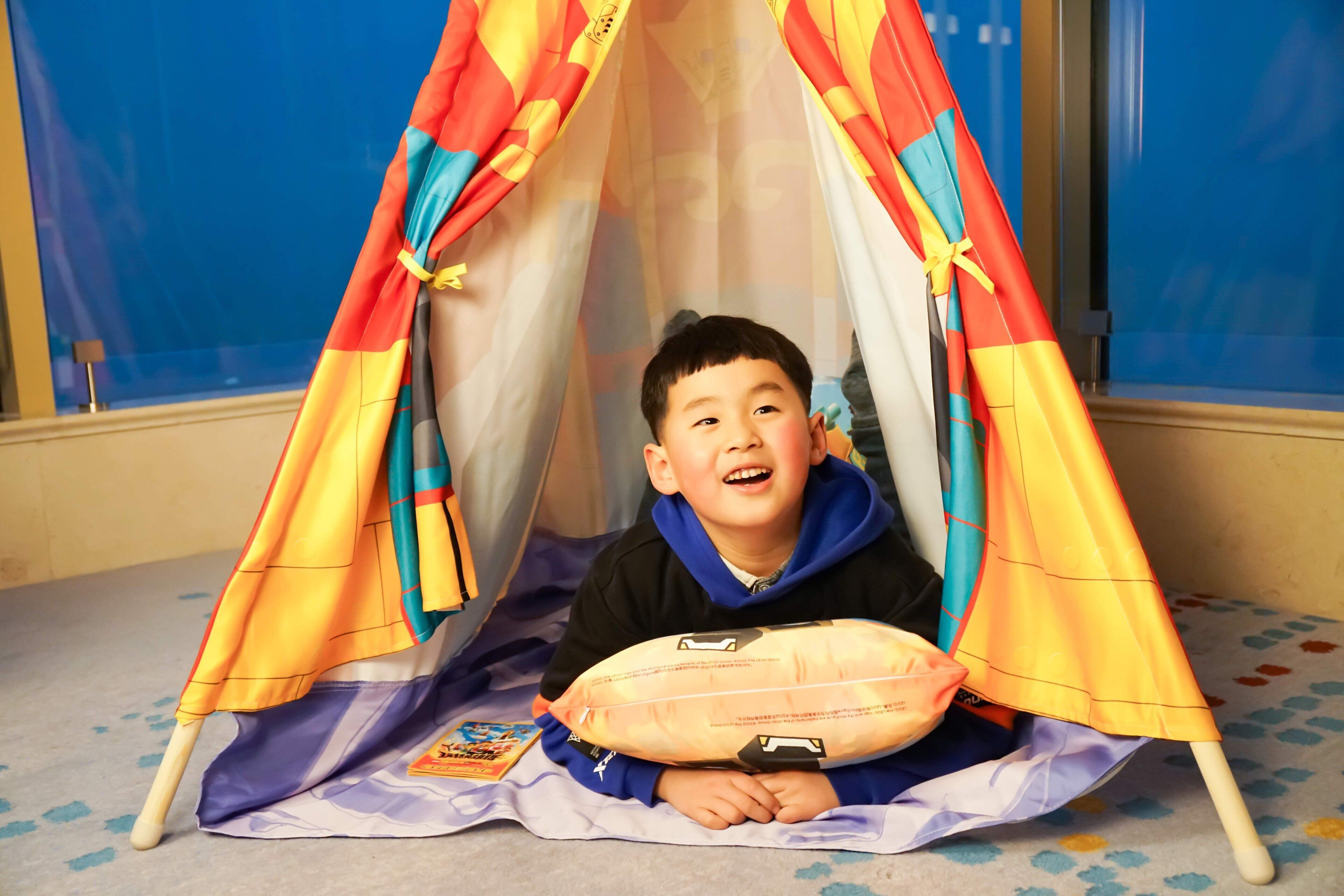 A child sitting inside a colorful tent-like structure on a carpeted floor.