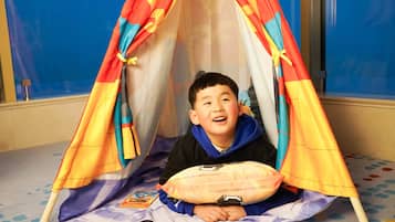 A child sitting inside a colorful tent-like structure on a carpeted floor.