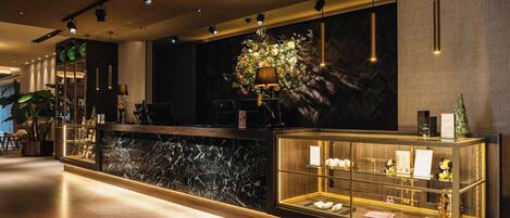 A hotel reception area with a marble counter, a display case with items, and a large floral arrangement on the wall.