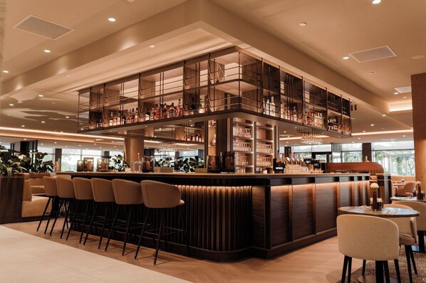 Un espace bar moderne avec un plafond haut, des tabourets de bar et une variété de bouteilles et de verres.