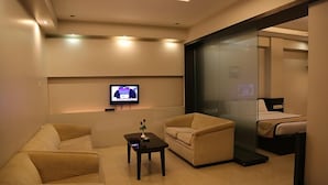 Une chambre d’hôtel moderne, équipée d’un canapé, d’une petite table avec un vase, d’un lit et d’un téléviseur fixé au mur.