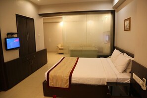 A hotel room with a bed, a TV mounted on the wall, a wardrobe, and a sliding glass door leading to a balcony. - The Curzon Court (Bengaluru)