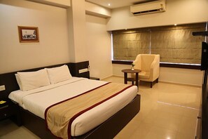 A hotel room with a large bed, a chair, a small table, and a large window with curtains. - The Curzon Court (Bengaluru)