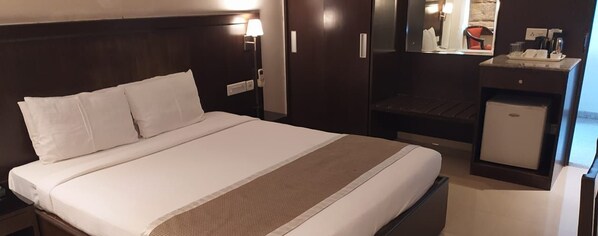 A hotel room with a large bed, a bedside table with a lamp, a small desk with a computer, and a mirror.