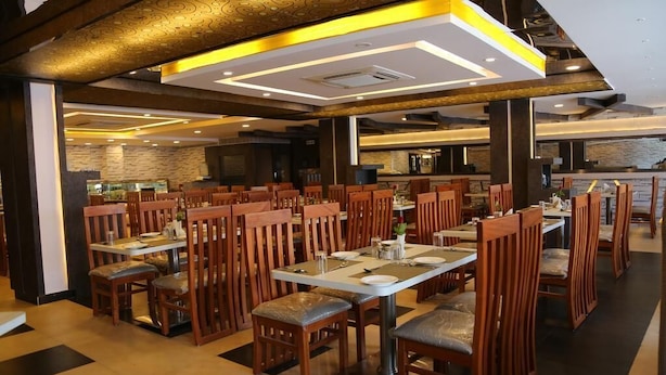 Un restaurant spacieux avec des chaises et des tables en bois, un mur en pierre en arrière-plan et un design moderne au niveau du plafond.