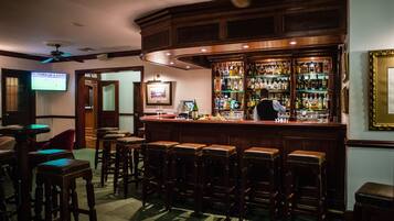 A bar area with wooden stools, a bar counter, and a television screen mounted on the wall.