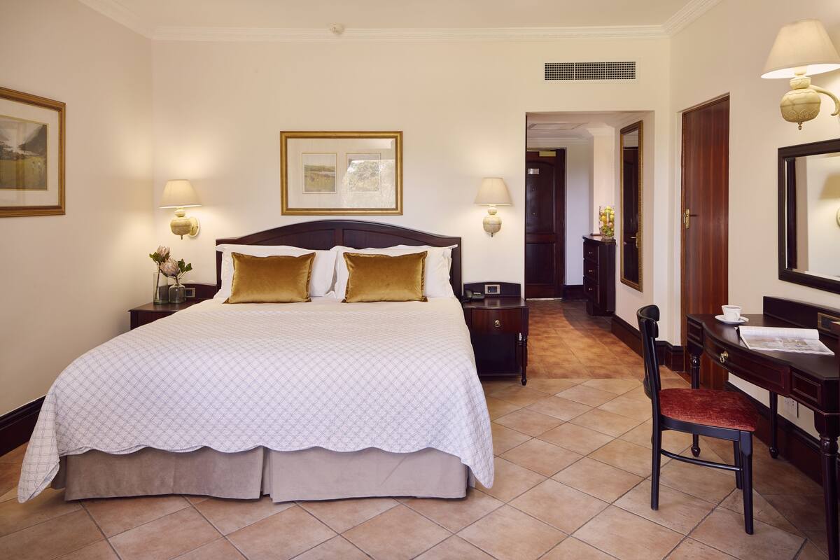 A hotel room with a large bed, two bedside tables with lamps, a desk with a chair, and a mirror.