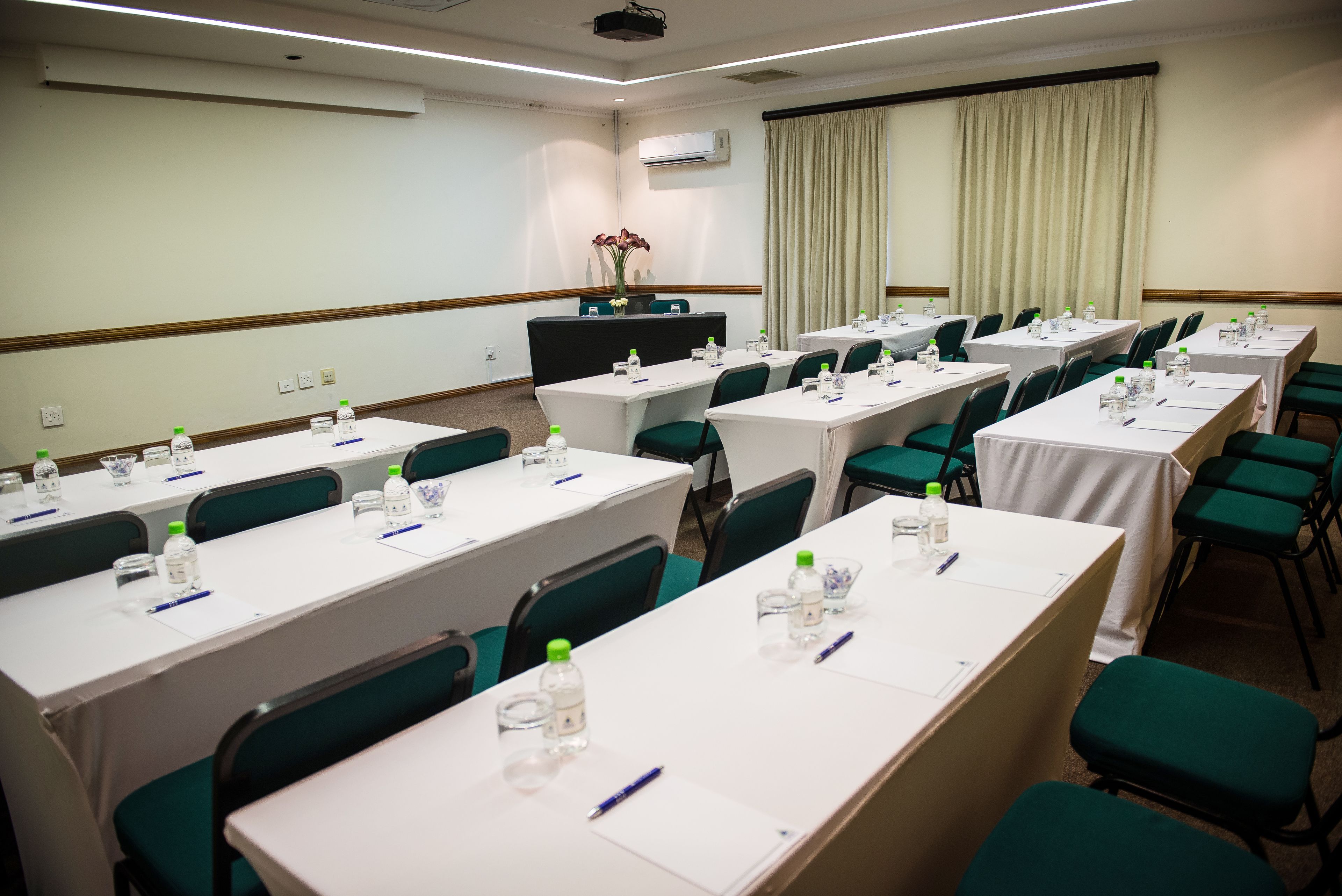 A conference room with multiple tables, each equipped with water bottles, pens, and notepads.