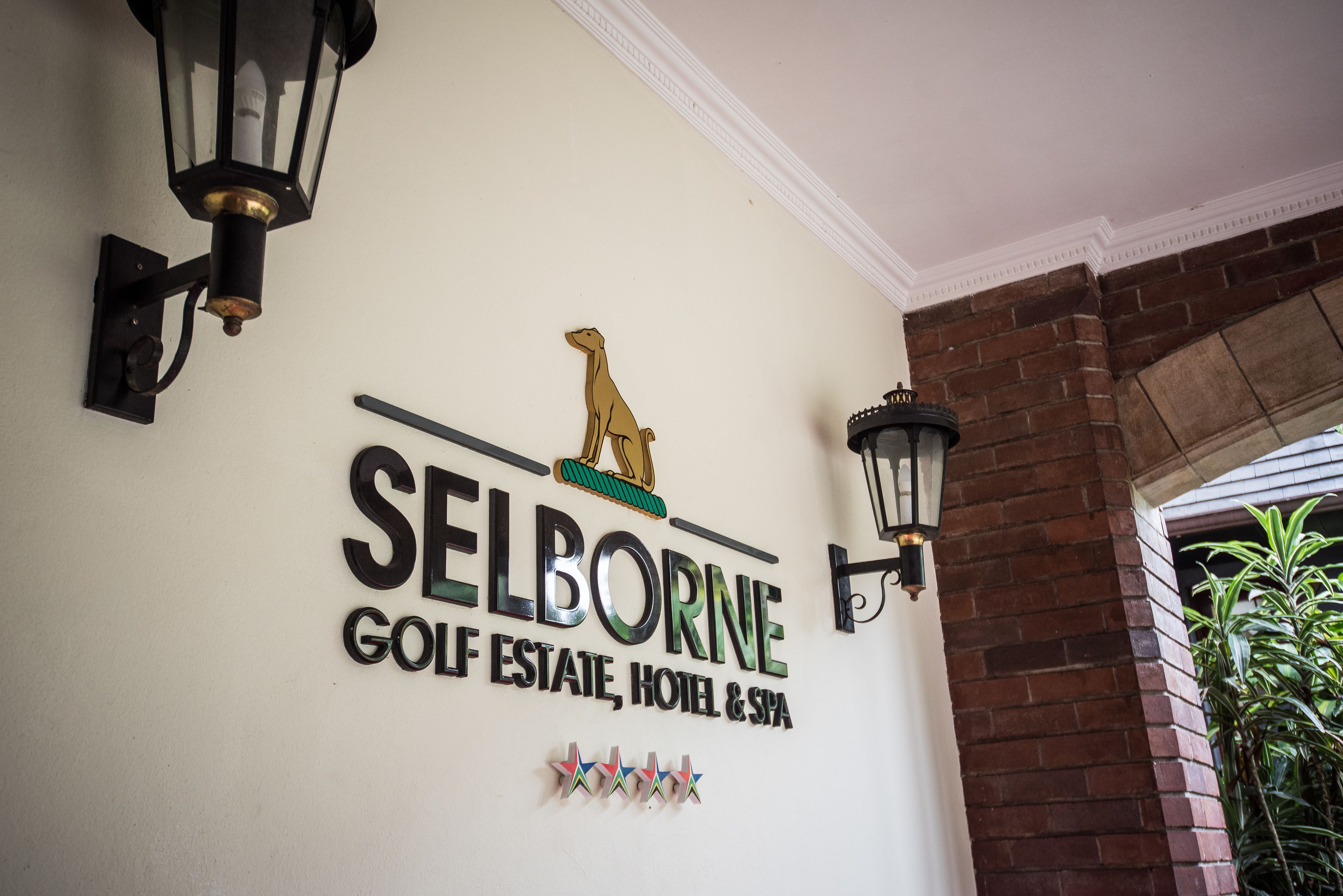 Letrero de pared para 'Selborne Golf Estate, Hotel & Spa' con un logotipo, elementos decorativos y dos faroles de pared.
