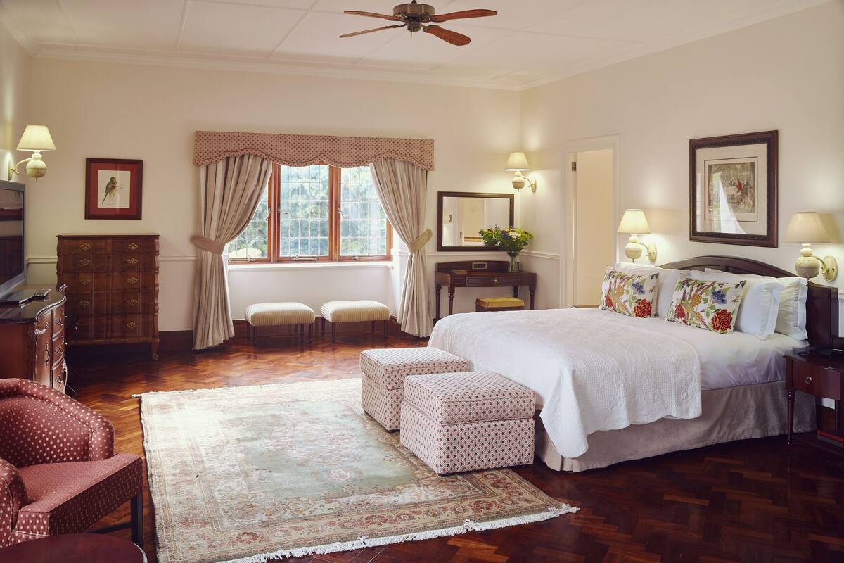 A bedroom with a large bed, a wooden dresser, a chair, a desk, and a window with curtains.