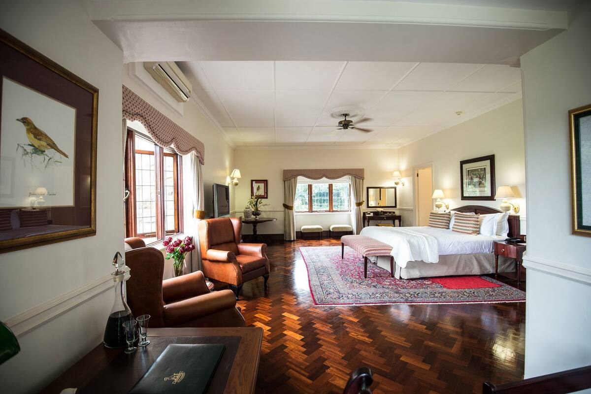 A hotel room with a bed, a chair, a desk, a window with curtains, and a ceiling fan.