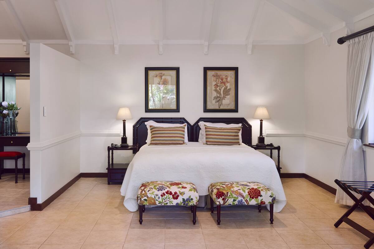 A hotel room with a large bed, two bedside tables with lamps, a desk with a chair, and a window with curtains.