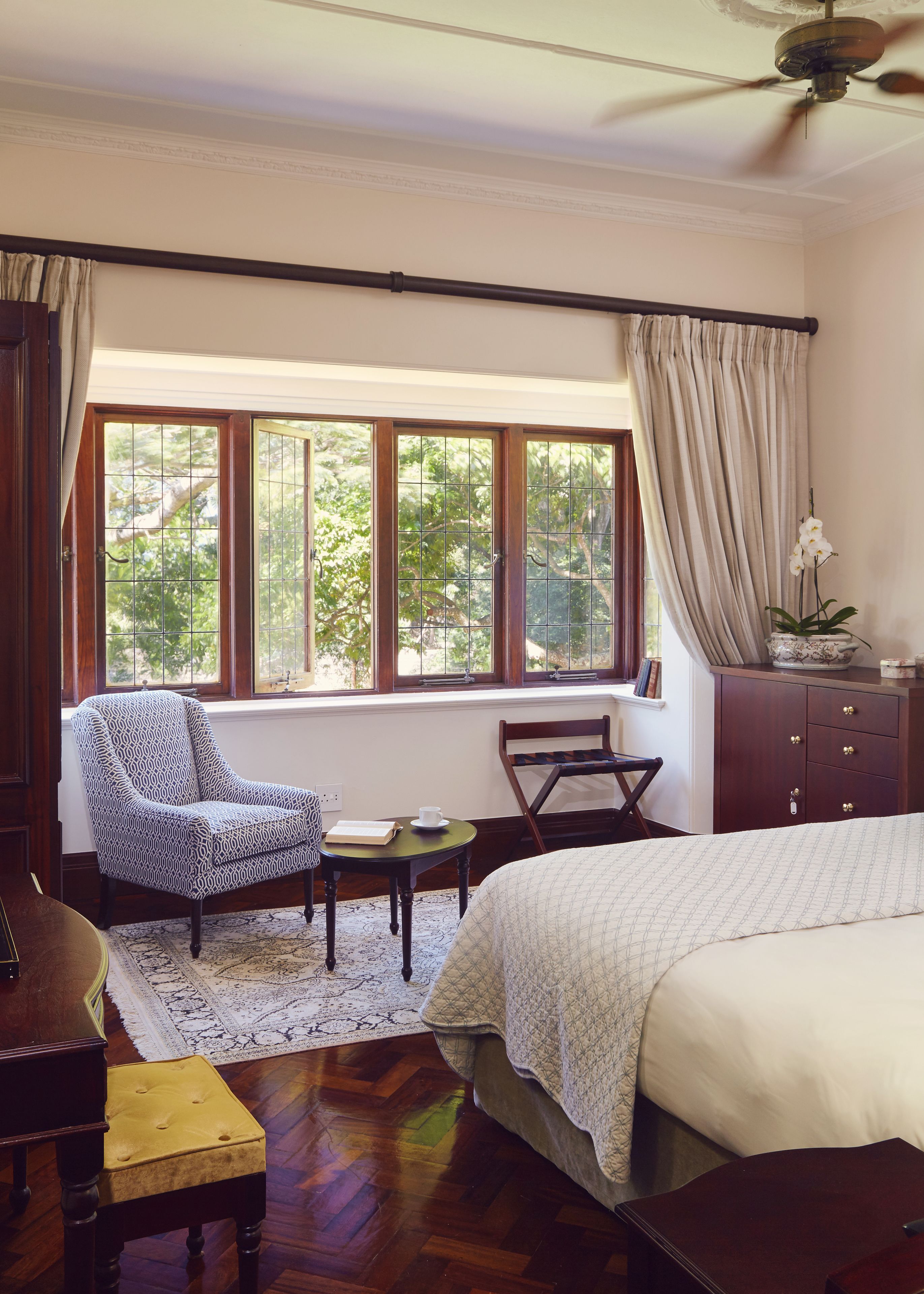A bedroom with a large bed, a chair, a small table, and a window with curtains.