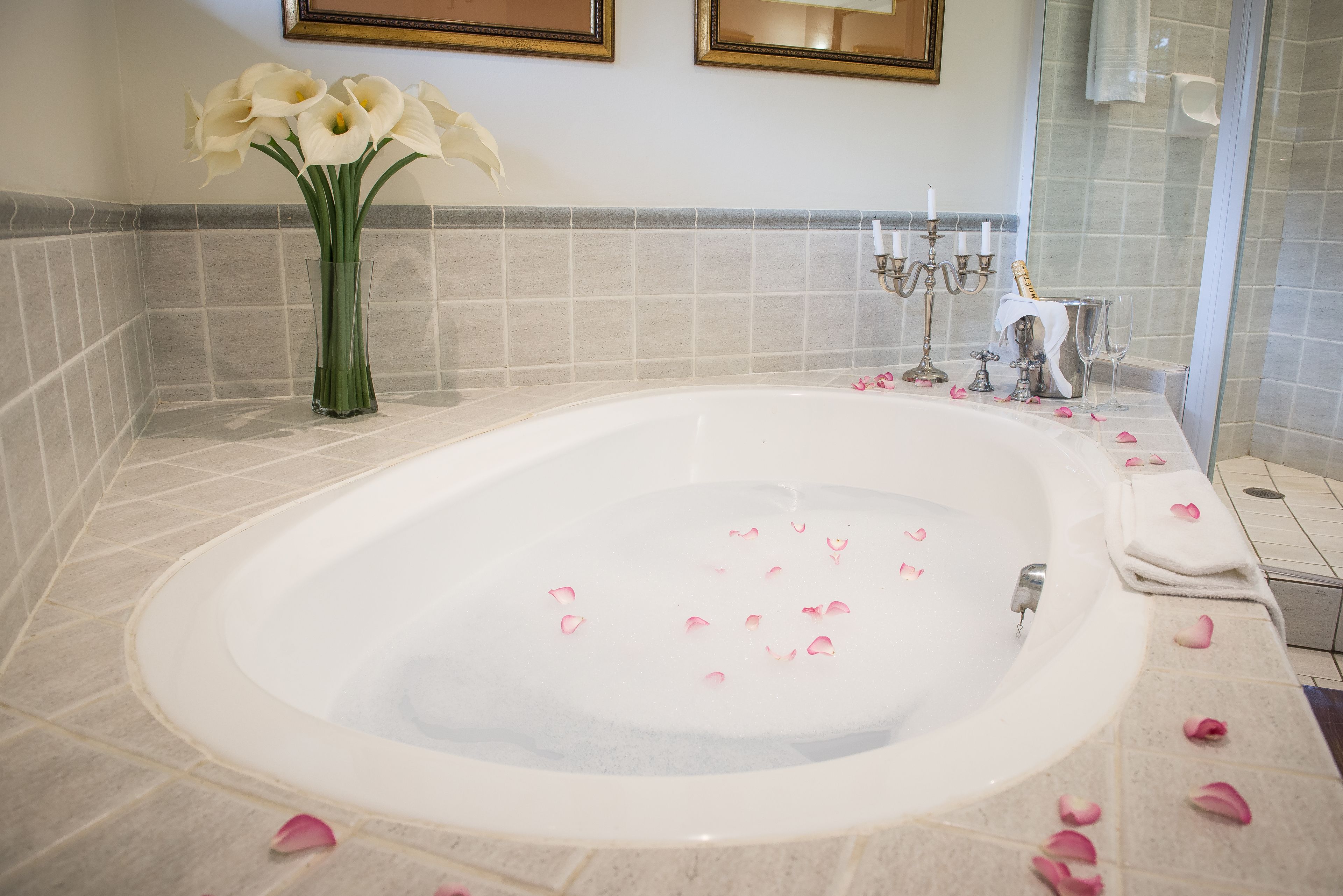 Un baño con una bañera grande, paredes con azulejos, un jarrón con flores y un espejo.