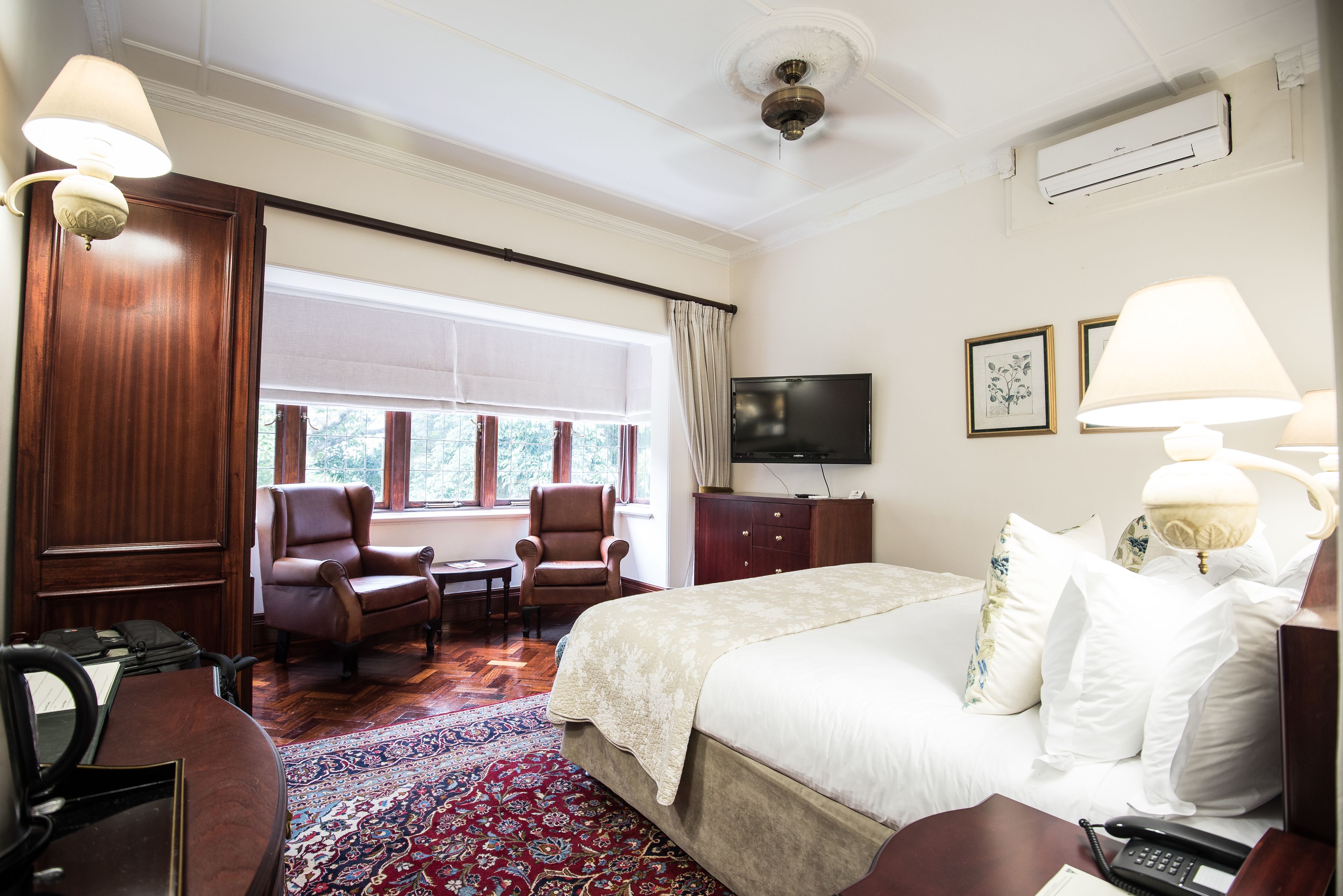 Ein Hotelzimmer mit einem großen Bett, zwei Sesseln, einem Schreibtisch, einem Fernseher und einem fenster mit Vorhängen.