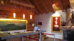 A reception area with a wooden wall, a painting of mountains, a clock, and a framed picture of a flower. - Sierralta Hotel Cabañas y Convenciones (Mazamitla)