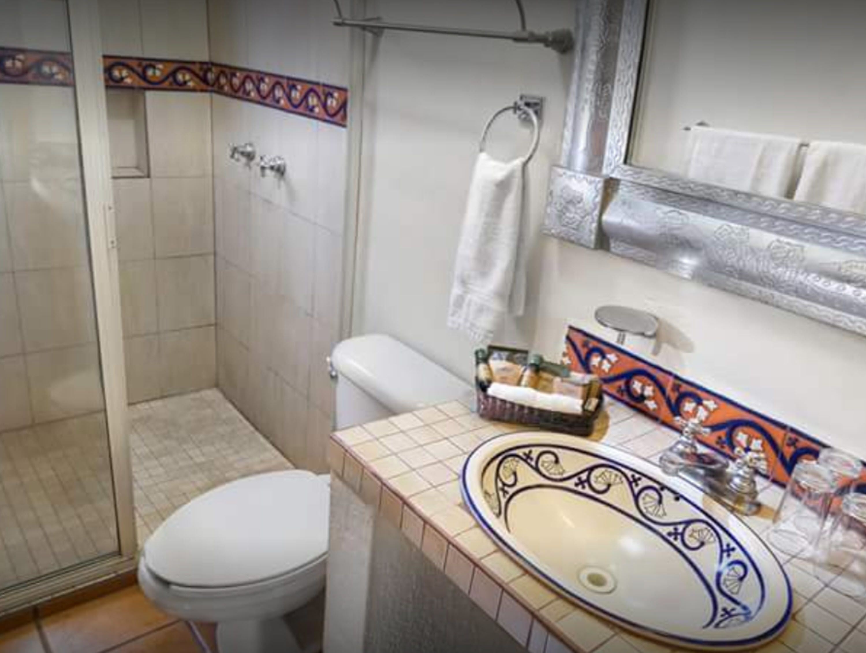 Une salle de bain comprenant des toilettes, un lavabo agrémenté de carreaux décoratifs, un espace douche et un porte-serviettes.