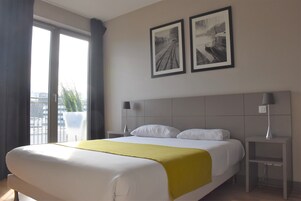 Camera d'albergo con un letto grande, due comodini con lampade, una finestra con tende e due quadri appesi al muro.