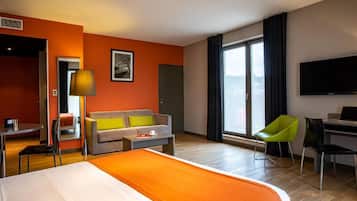 Ein Hotelzimmer mit Bett, Sofa, Schreibtisch, Stuhl, Fernseher und einem großen Fenster mit Blick.