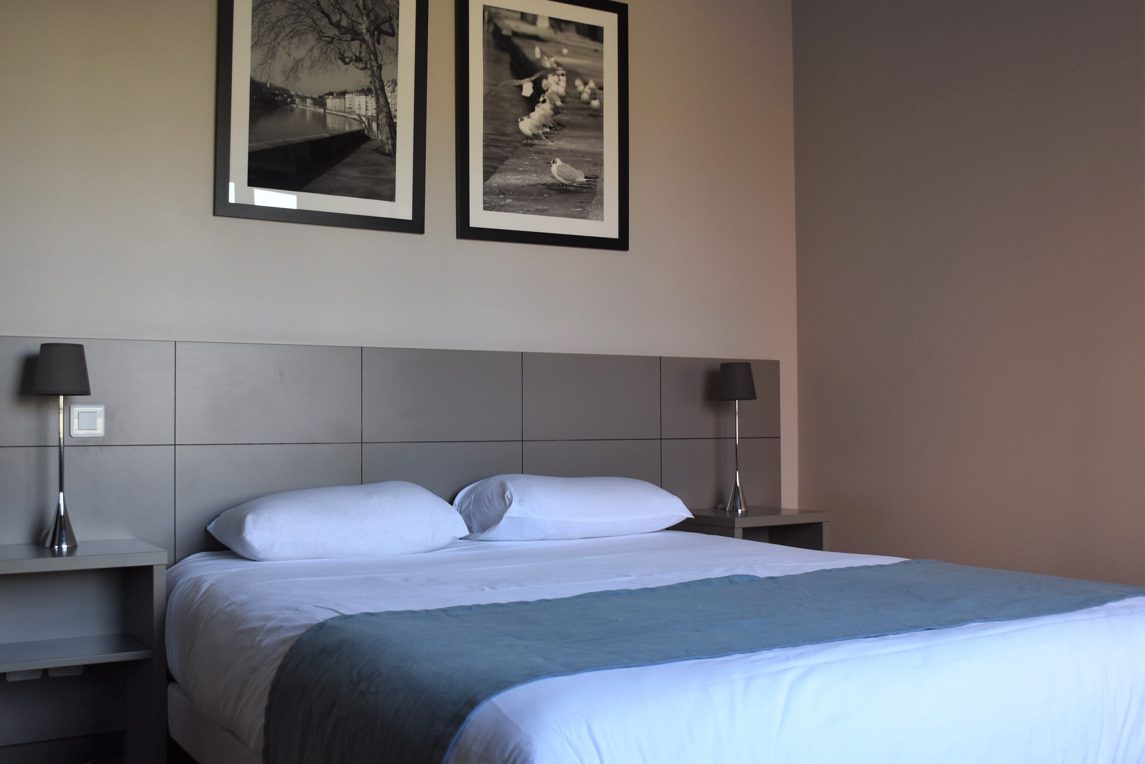Una camera d'albergo con un letto, due comodini, due quadri appesi alla parete e una lampada su ciascun comodino.