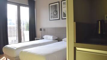 A hotel room with two beds, a large window with curtains, a flat-screen TV, and framed pictures on the wall.