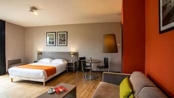 A hotel room with a bed, a sofa, a coffee table, a desk with chairs, and a lamp.